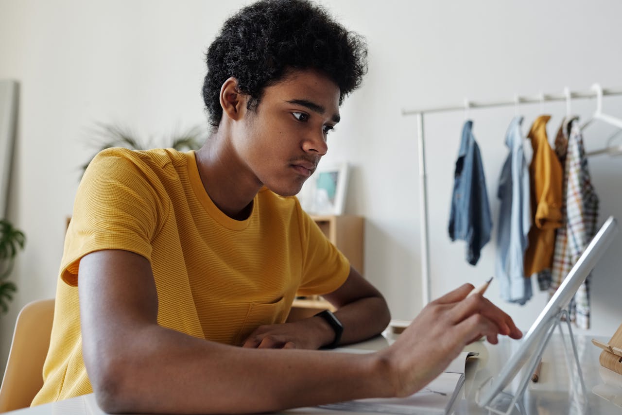 Teenage boy engaged in online learning using a tablet indoors.