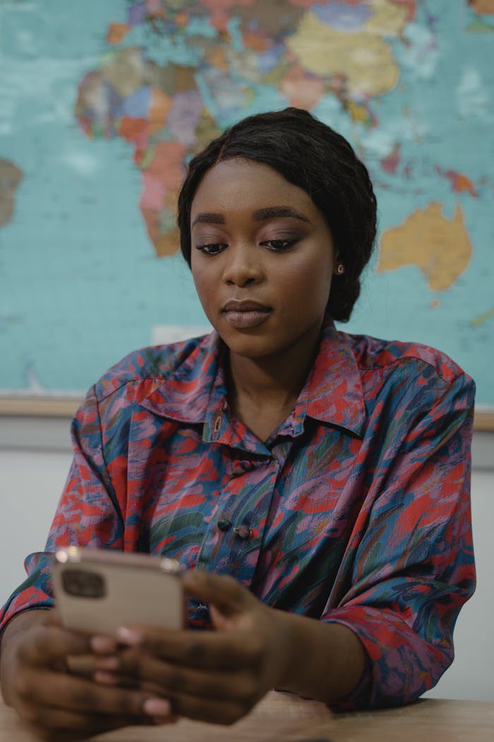 Black woman in a classroom browsing a smartphone, map background.
