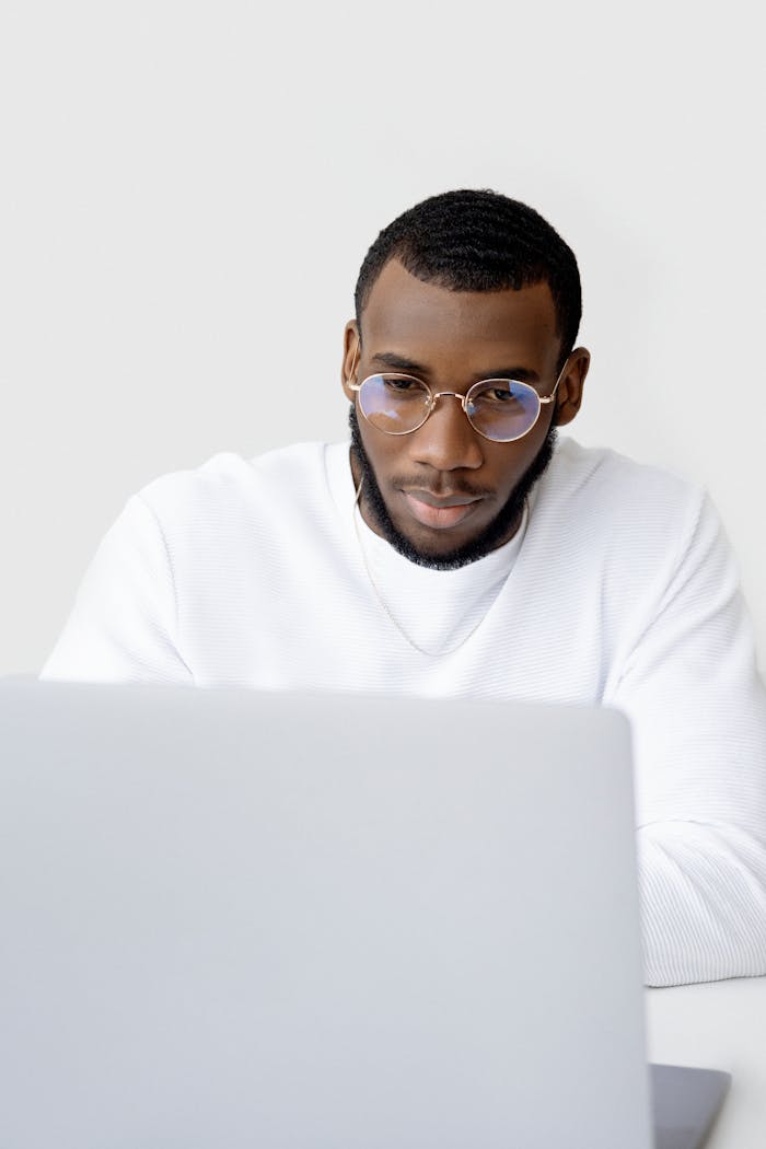 Young man in glasses and sweater working at a laptop with a focused expression.